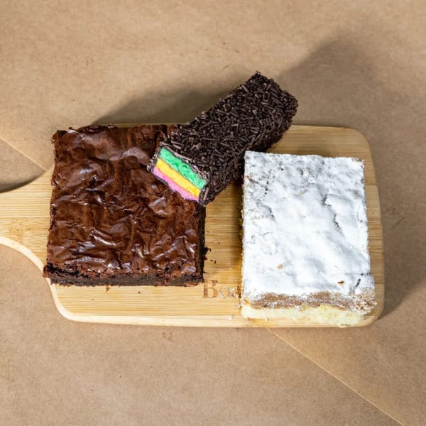 A brownie, rainbow cookie, and powdered sugar pastry on a wooden board.
