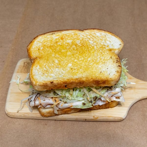 NY Slicers Deli sandwich with toasted bread, sliced turkey, and shredded lettuce on a wooden board.