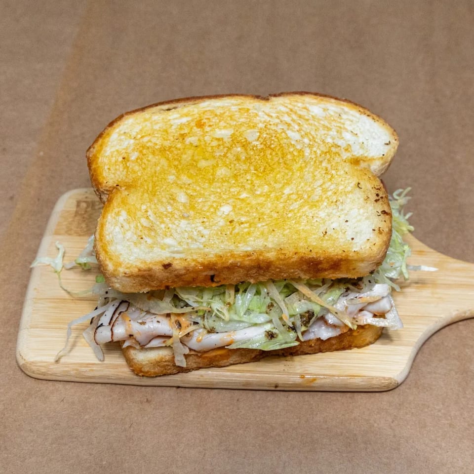 NY Slicers Deli sandwich with toasted bread, sliced turkey, and shredded lettuce on a wooden board.